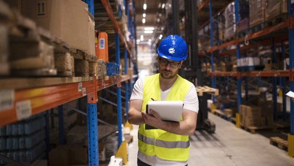 Warehouse worker writing down inventory report on products in large storage area.